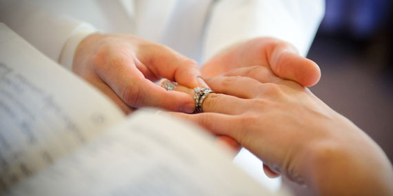 Groom putting wedding ring on bride during chapel wedding